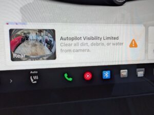 Tesla skærm viser advarsel om begrænset autopilot synlighed og opfordrer til at rense kameraet.