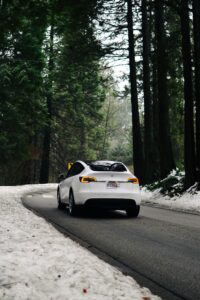 Hvid Tesla kører gennem sneklædt skovlandskab