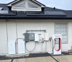 Tesla hjemmelader og solpanelkontrolsystem installeret på husvæg.