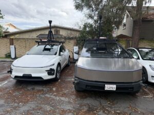 To Tesla-biler med avanceret sensorteknologi parkeret ved ladestationer, omgivet af natur og moderne huse