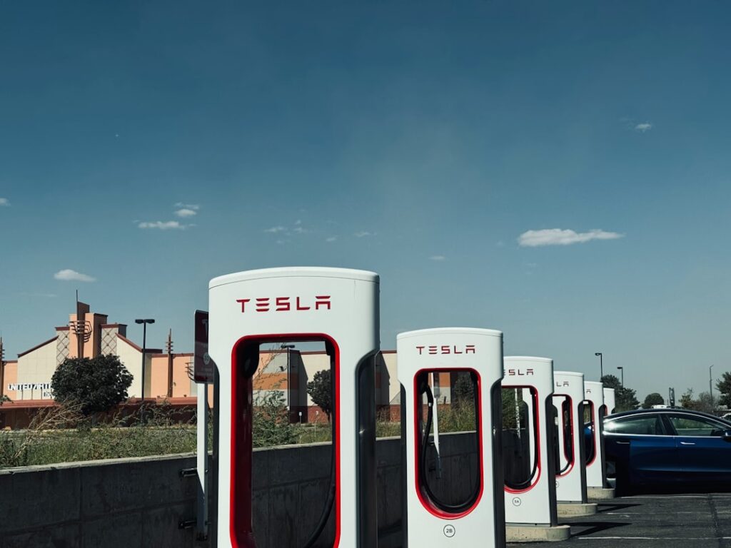 Tesla ladestationer på række med blå bil ved siden af, under en skyfri himmel