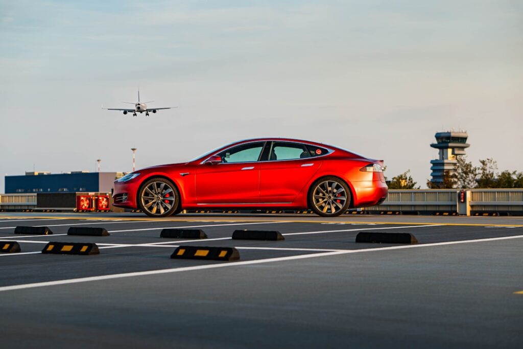 Rød Tesla Model S parkeret på en lufthavnsparkering med et fly i baggrunden