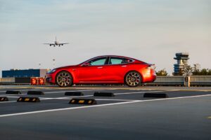 Rød Tesla Model S parkeret på en lufthavnsparkering med et fly i baggrunden