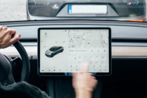 Person interagerer med Tesla Model 3's touchskærm i bilens instrumentbræt.