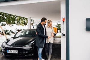 Par betragter Tesla elbil under opladning hjemme i carporten