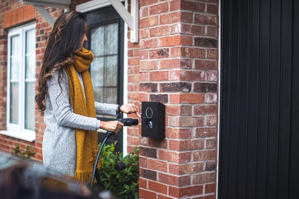 Kvinde oplader elektrisk bil ved ladestation hjemme