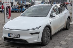Hvid Tesla Model Y af den nye generation parkeret foran en Tesla Supercharger