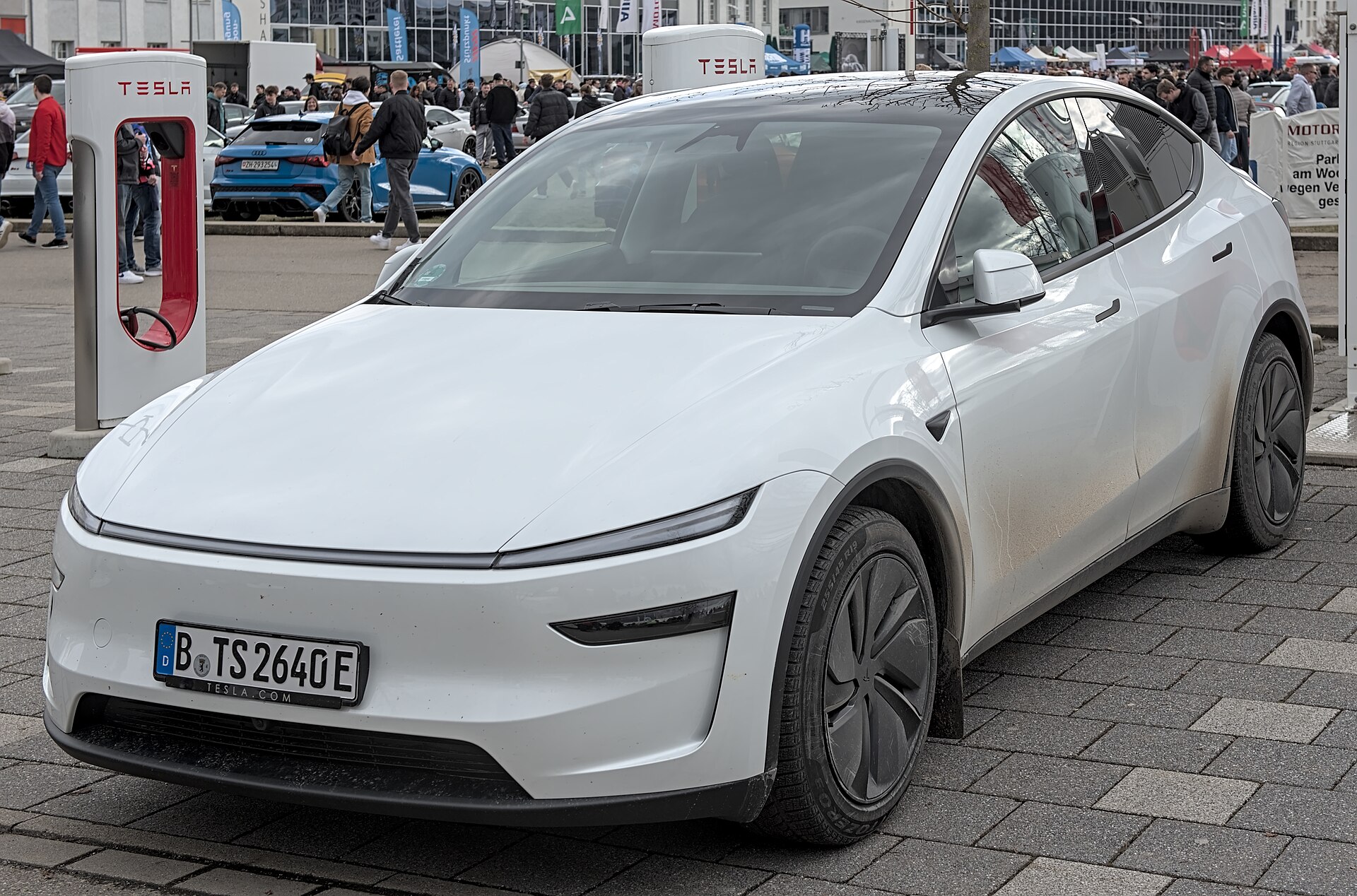 Hvid Tesla Model Y af den nye generation parkeret foran en Tesla Supercharger
