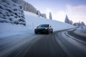 Mørk Tesla Model 3 kører på en ryddet bjergvej med sne i vejkanten