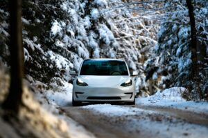 Hvid Tesla Model 3 kører på en snedækket skovvej med tændte forlygter