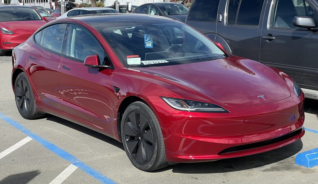 Rød Tesla Model 3 af den nye generation set skråt forfra på en parkeringsplads