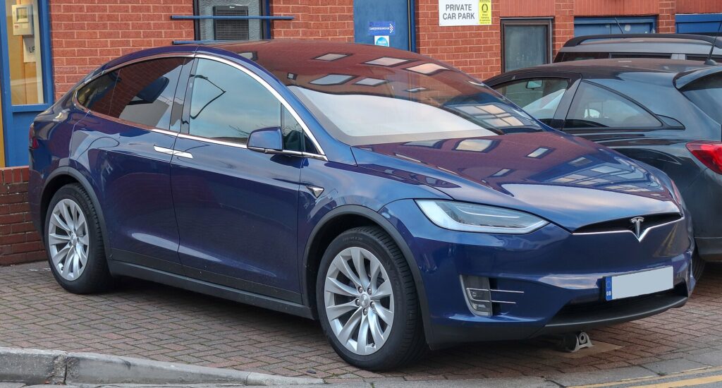 Blå Tesla Model X 100D fra 2018 parkeret foran en murstensbygning
