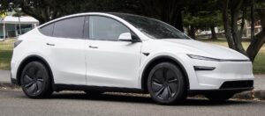 Hvid Tesla Model Y af den nye generation med baghjulstræk set skråt forfra, parkeret ved en vej med træer