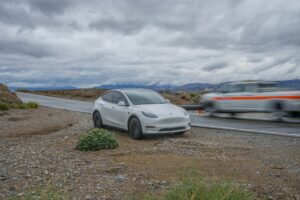 Hvid Tesla Model Y af første generation parkeret i vejkanten ved en landevej med bjerge i baggrunden