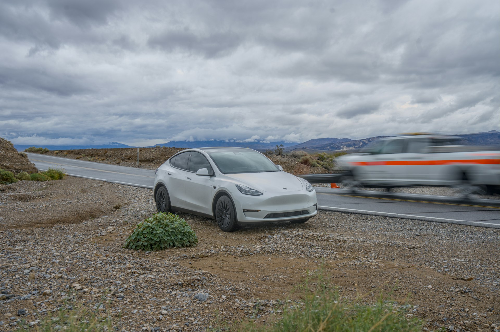Hvid Tesla Model Y af første generation parkeret i vejkanten ved en landevej med bjerge i baggrunden